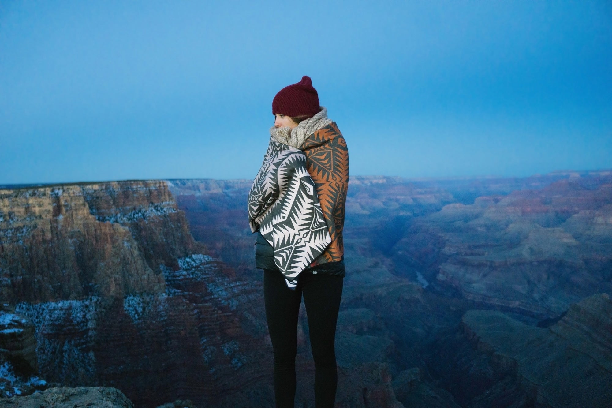 Person wrapped in patterned blankets overlooking a canyon landscape