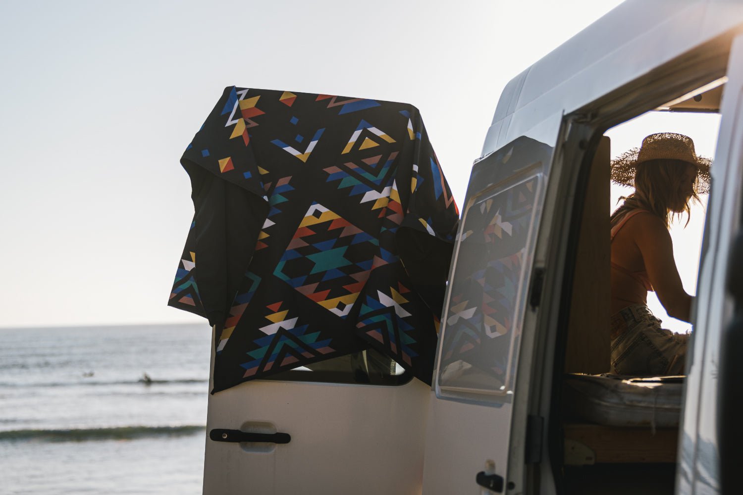 Patterned towel draped over a van door beside the ocean with a person inside