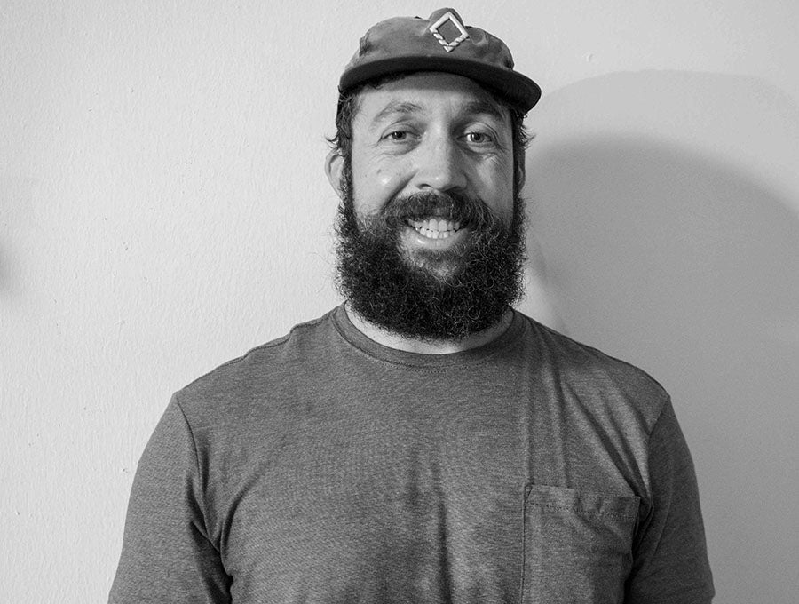 Hunter Robinson smiling at the camera in a black-and-white portrait, wearing a cap and T-shirt against a plain wall