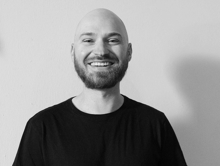 Portrait of Nomadix co-founder Zack Helminiak smiling in a black shirt against a plain wall