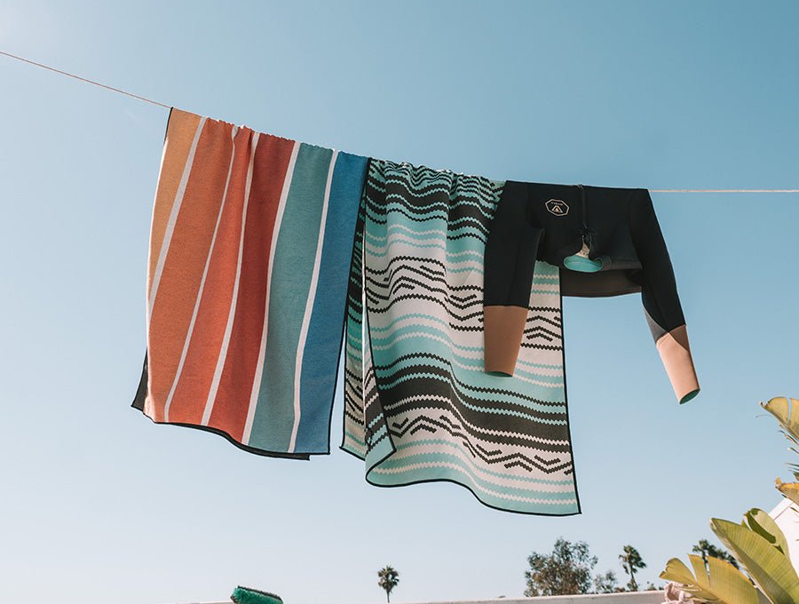 Laundry drying on a clothesline outdoors, including striped towels and a black long-sleeve garment against a blue sky