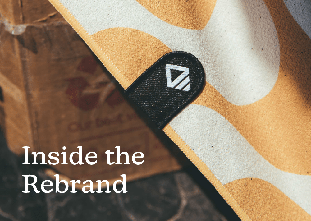 Close-up of a patterned Nomadix towel showcasing logo patch on a wooden surface with headline Inside the Rebrand