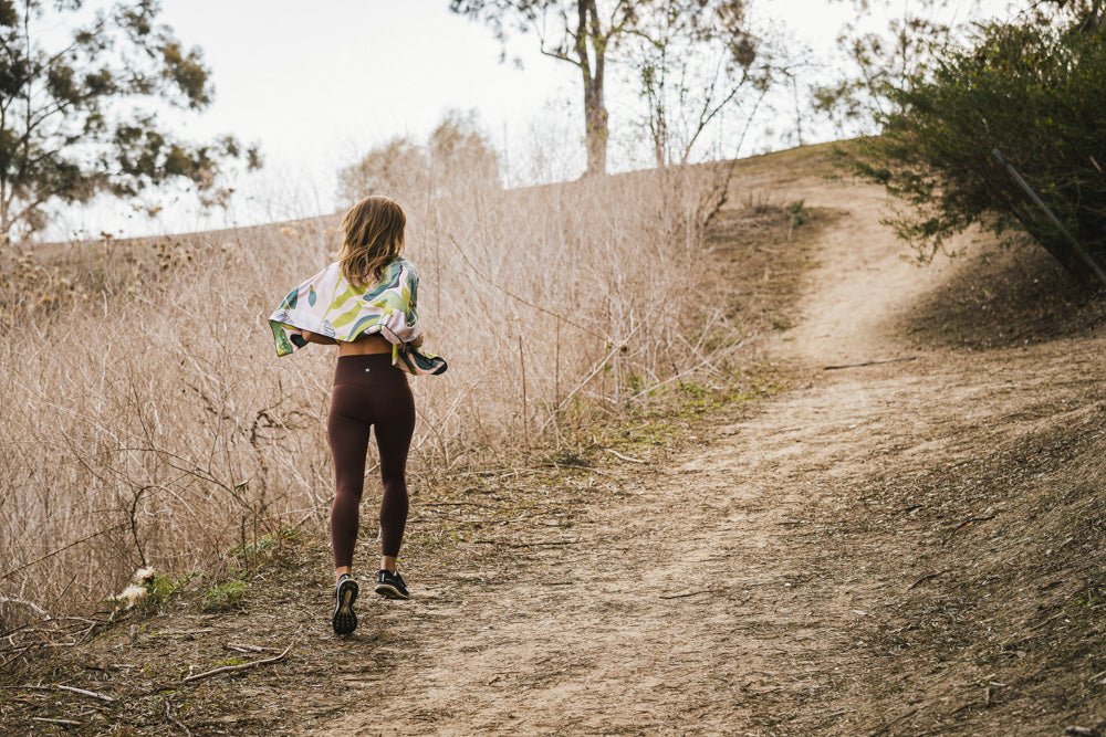 Woman walking along a wooded dirt trail with a colorful towel draped around her shoulders