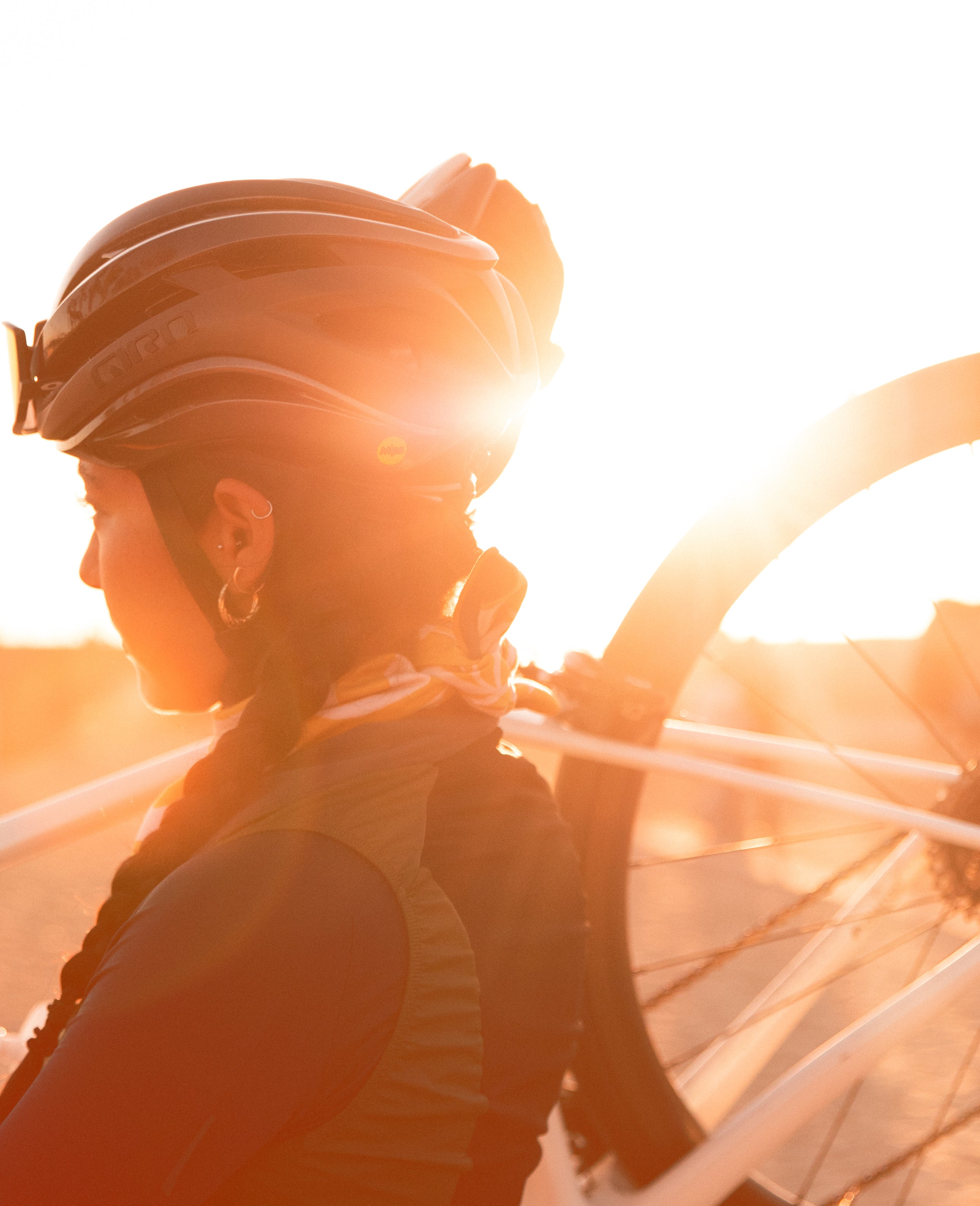 Gemma Bachmann rides a bicycle across a sunlit bridge wearing a helmet
