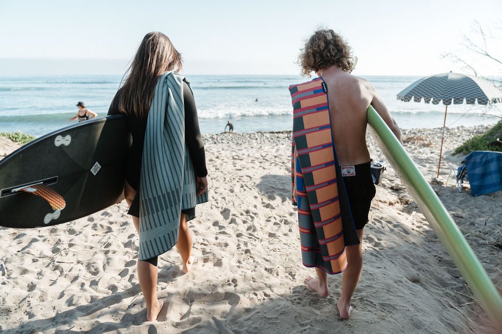 Two surfers carrying surfboards toward the ocean on a sandy beach