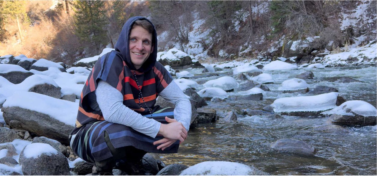 Cameron LaBar crouching beside a partially frozen creek in a snowy forest