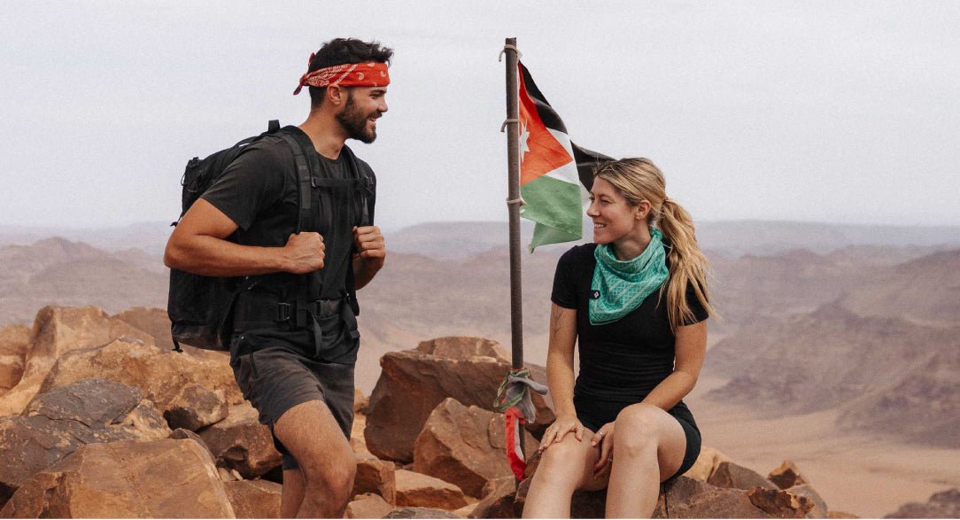 Travelers hiking on a rocky mountain beside a Jordanian flag with desert mountains in the background