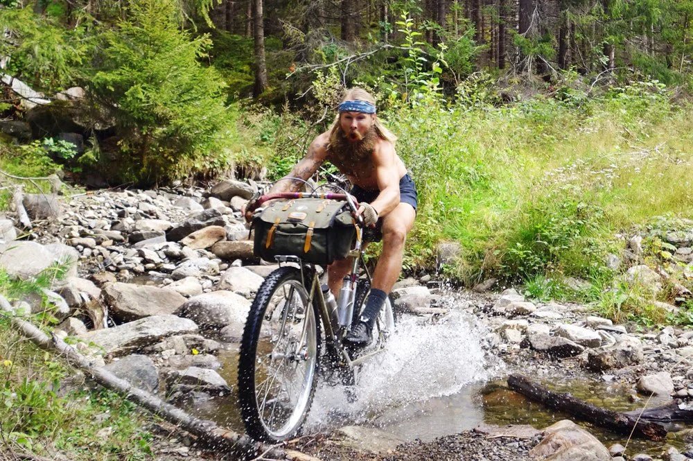Cyclist rides a loaded bike through a rocky forest stream while bikepacking