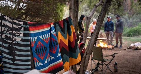 People hanging around a campfire in the background while Nomadix towels hang in the foreground.