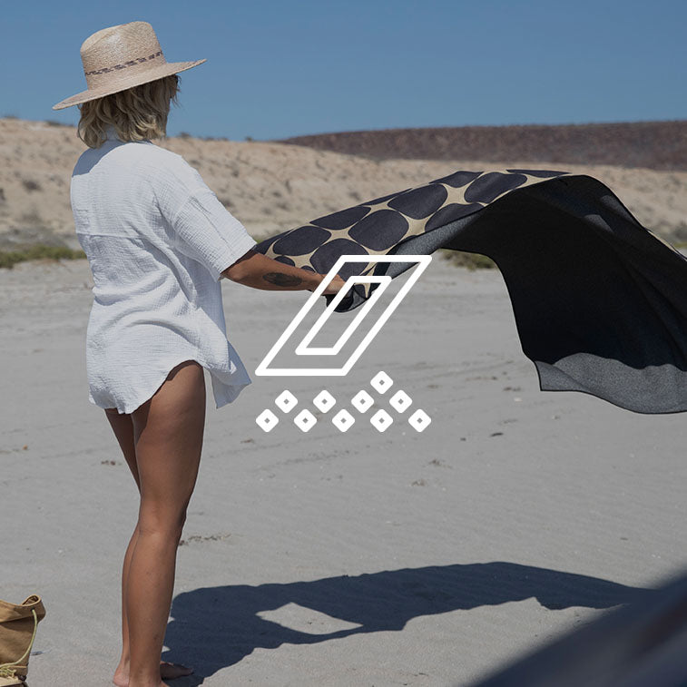 A person shaking the sand off of a Nomadix towel.